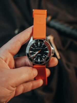 A modern wristwatch with an orange strap held by an adult's hand, showcasing stylish design.