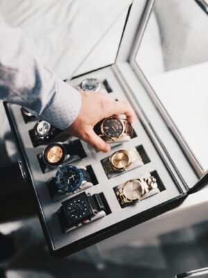 A sophisticated display of luxury watches in an elegant case with a hand selecting one.